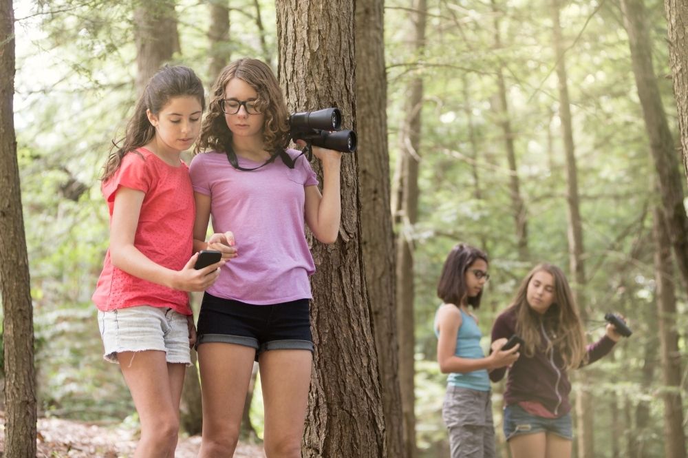 homeschool girls hiking in the woods with binoculars and journals